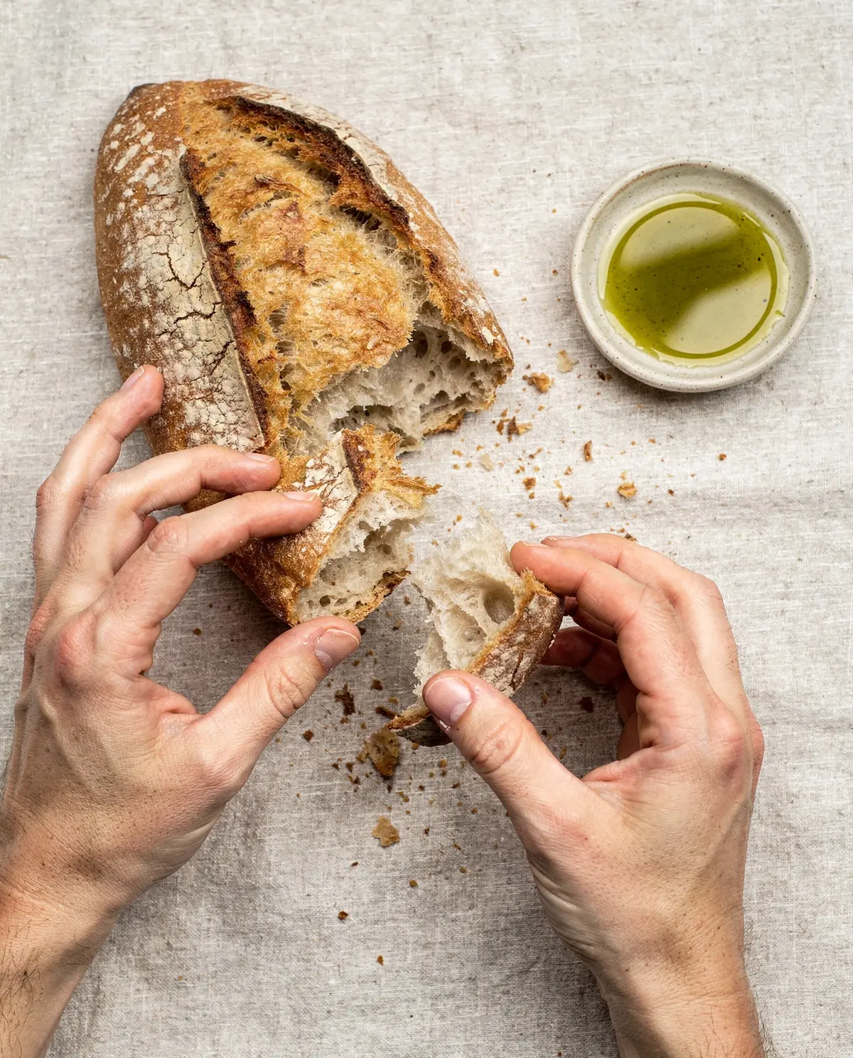 Hands tearing bread over linen
